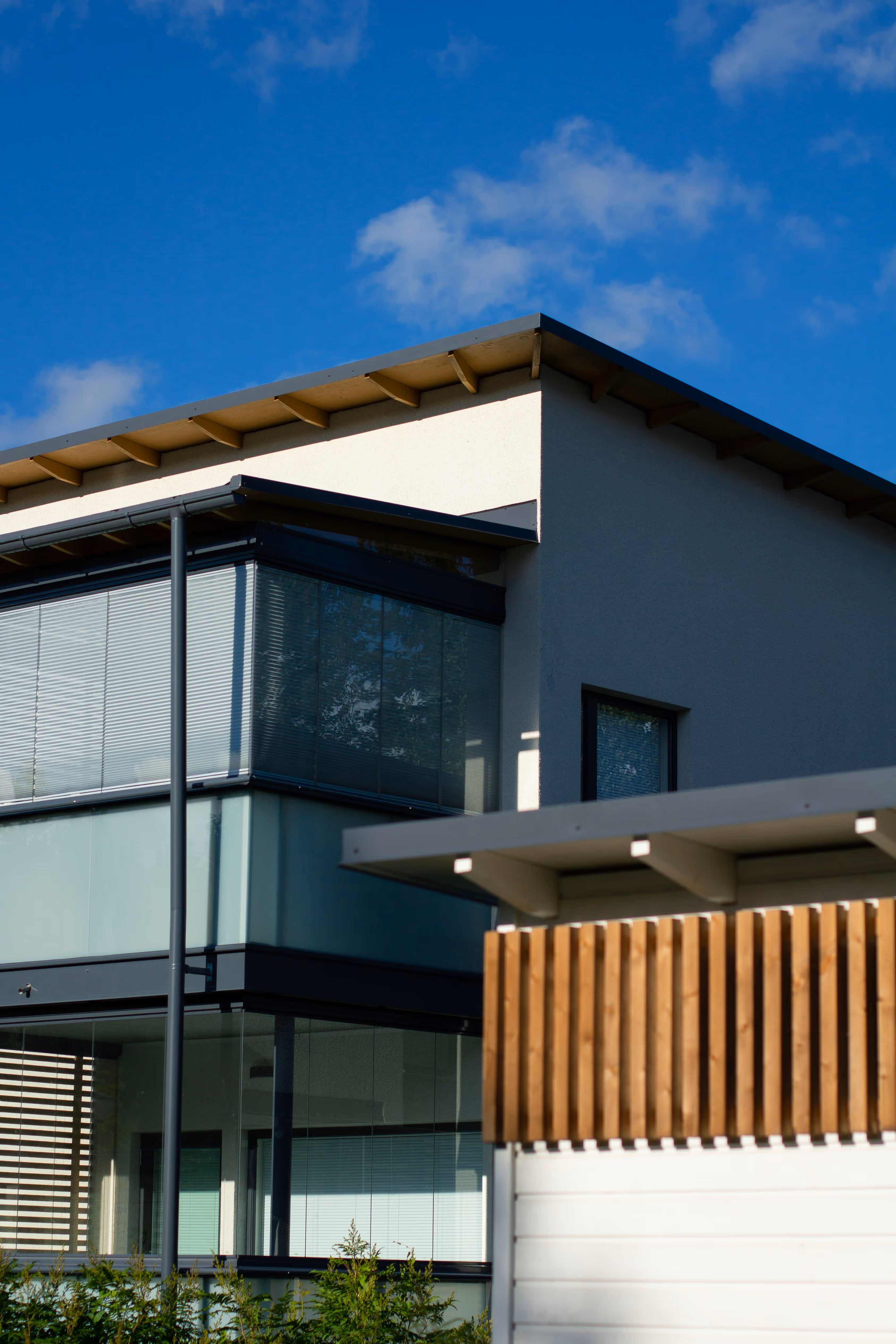 Modern two-story house with large windows and a white exterior under a blue sky with scattered clouds.